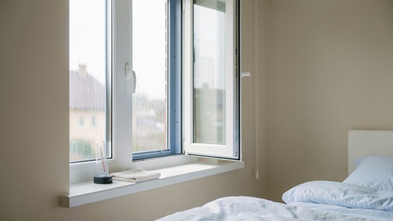 Chambre lumineuse avec de nouvelles fenêtres couvertes de condensation, une fenêtre entrouverte et un chiffon posé sur le rebord.