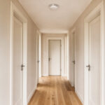 Intérieur de maison contemporain avec un détecteur de fumée fixé au plafond d’un couloir lumineux et des portes de chambres en arrière-plan.